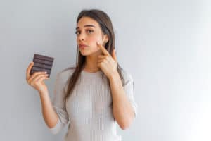 Young woman with problem skin holding chocolate bar