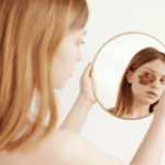 female with large brown spot on face under eye looking at mirror reflection