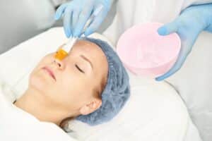Doctor’s gloved hands applying gel with a brush during a dermatology anti-aging treatment, part of a wrinkle reduction and aesthetic peeling therapy session using RF cosmetology techniques.
