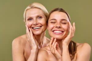 Young and mature women with clear, glowing skin standing against an olive background, representing skincare, spa treatments, plastic surgery, facelifts, and microdermabrasion.