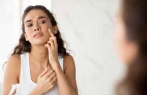 Woman looking in the mirror at her acne, trying to prevent scaring in Chevy Chase, MD